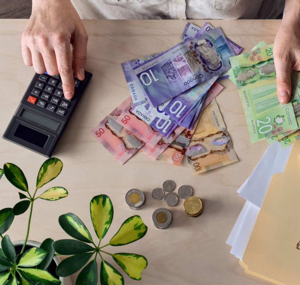 Person typing into calculator. There are Canadian bills and coins on the table.